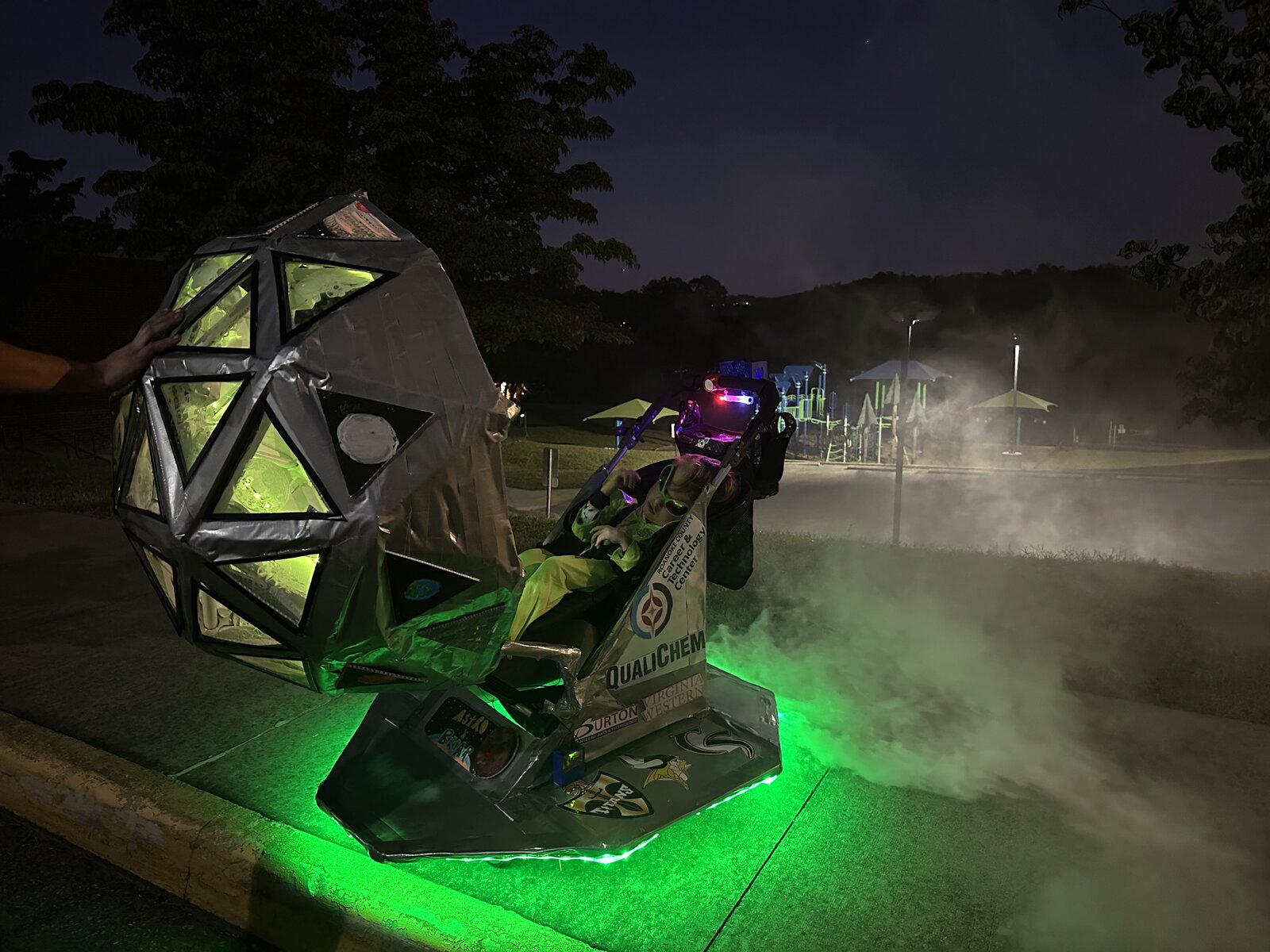 Alien spaceship costume on wheels glowing green with fog at night