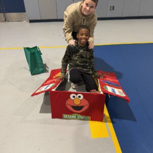 Child in an Elmo's World costume on wheels with the Timberlane Middle School students who built it