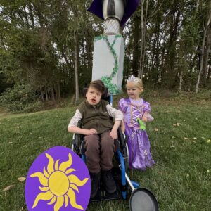 Child in a Flynn Rider with the Rapunzel Tower costume on wheels