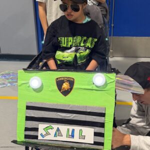 Child in a Lamborghini costume on wheels with the Timberlane Middle School students who built it