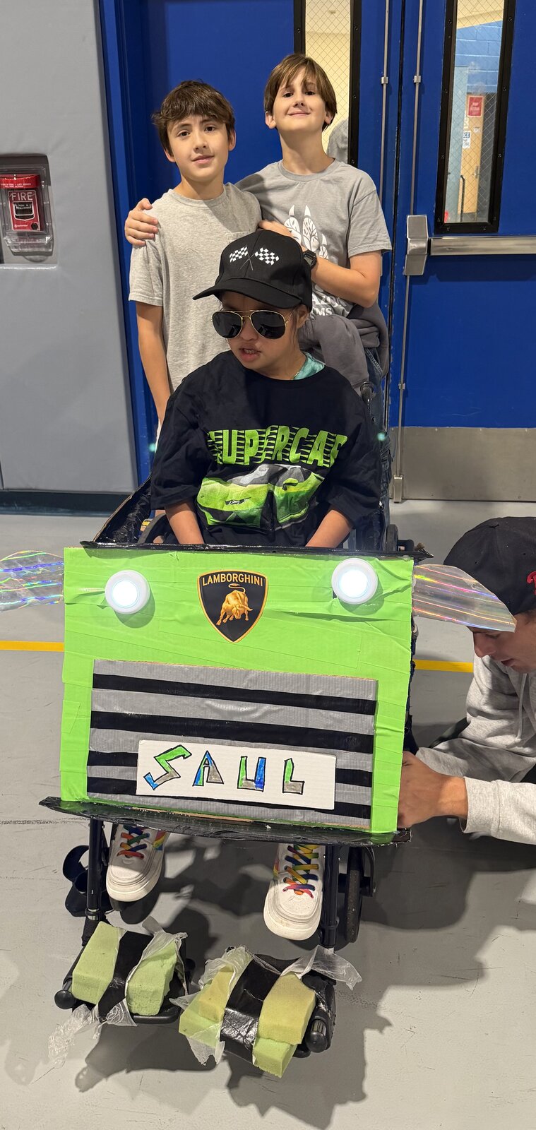 Child in a Lamborghini costume on wheels with the Timberlane Middle School students who built it