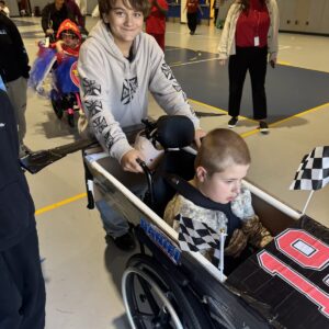 Child in a Race Car costume on wheels with the Timberlane Middle School students who built it