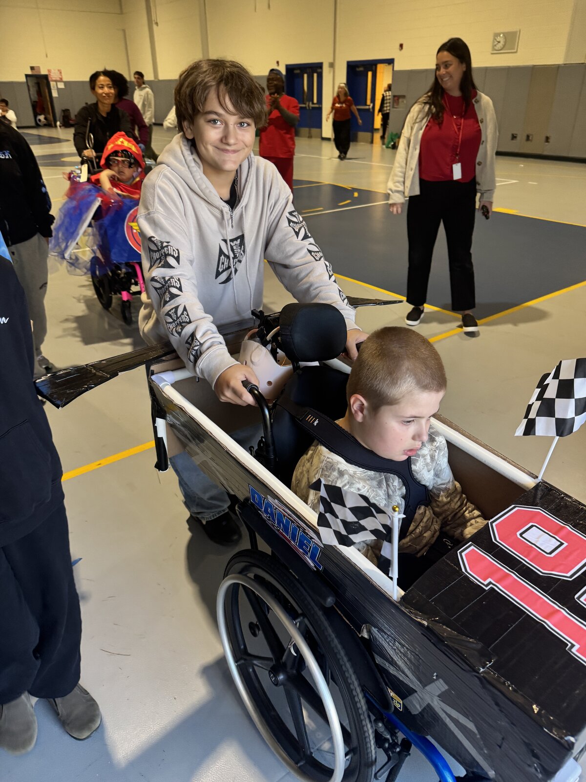 Child in a Race Car costume on wheels with the Timberlane Middle School students who built it