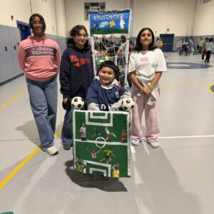 Child in a Soccer Player costume on wheels with the Timberlane Middle School students who built it