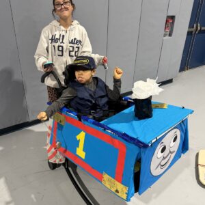 Child in a Thomas the Train costume on wheels with the Timberlane Middle School students who built it